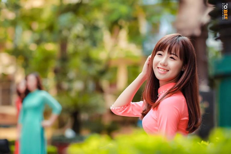 Nữ sinh mặc áo dài hồng pastel cười tươi khi chụp ảnh kỷ yếu ngoài trời