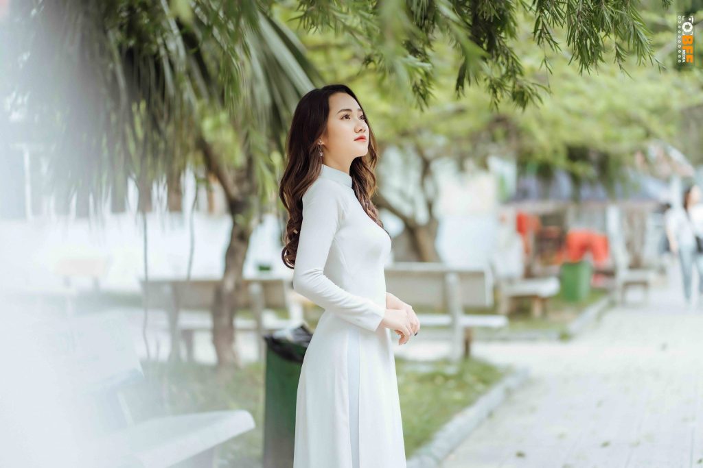 Nữ sinh mặc áo dài trắng chụp ảnh kỷ yếu dưới hàng cây trong sân trường