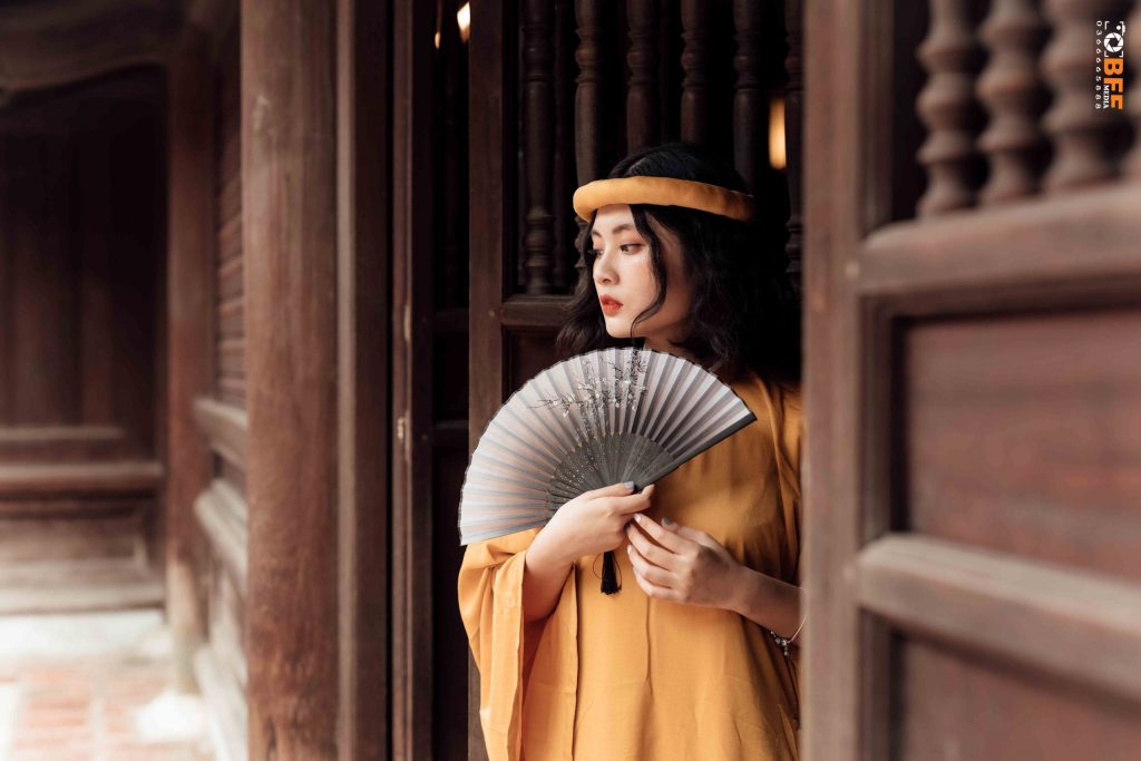 Áo dài màu vàng nghệ kết hợp quạt giấy, chụp kỷ yếu trong không gian nhà gỗ cổ