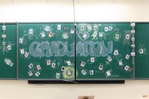 Bảng kỷ yếu chữ Graduation vẽ phấn, xung quanh gắn ảnh polaroid của lớp