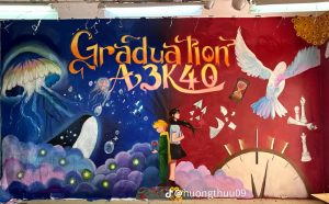 Tường kỷ yếu Graduation A3K40 vẽ cá voi, bồ câu và sách mở trên nền xanh đêm