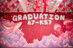 Trang trí lớp kỷ yếu Graduation A7-K57 vẽ cá voi và sứa hồng trên nền đỏ