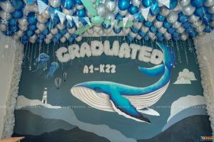 Trang trí lớp kỷ yếu concept đại dương: tường vẽ cá voi xanh, chữ Graduated A1-K22 và rèm sứa thả trần
