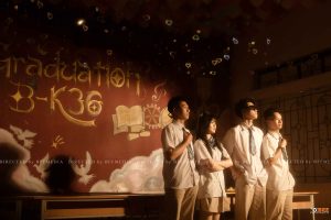 Nhóm học sinh chụp kỷ yếu trước tường Graduation B-K36 vẽ sách và chữ vàng