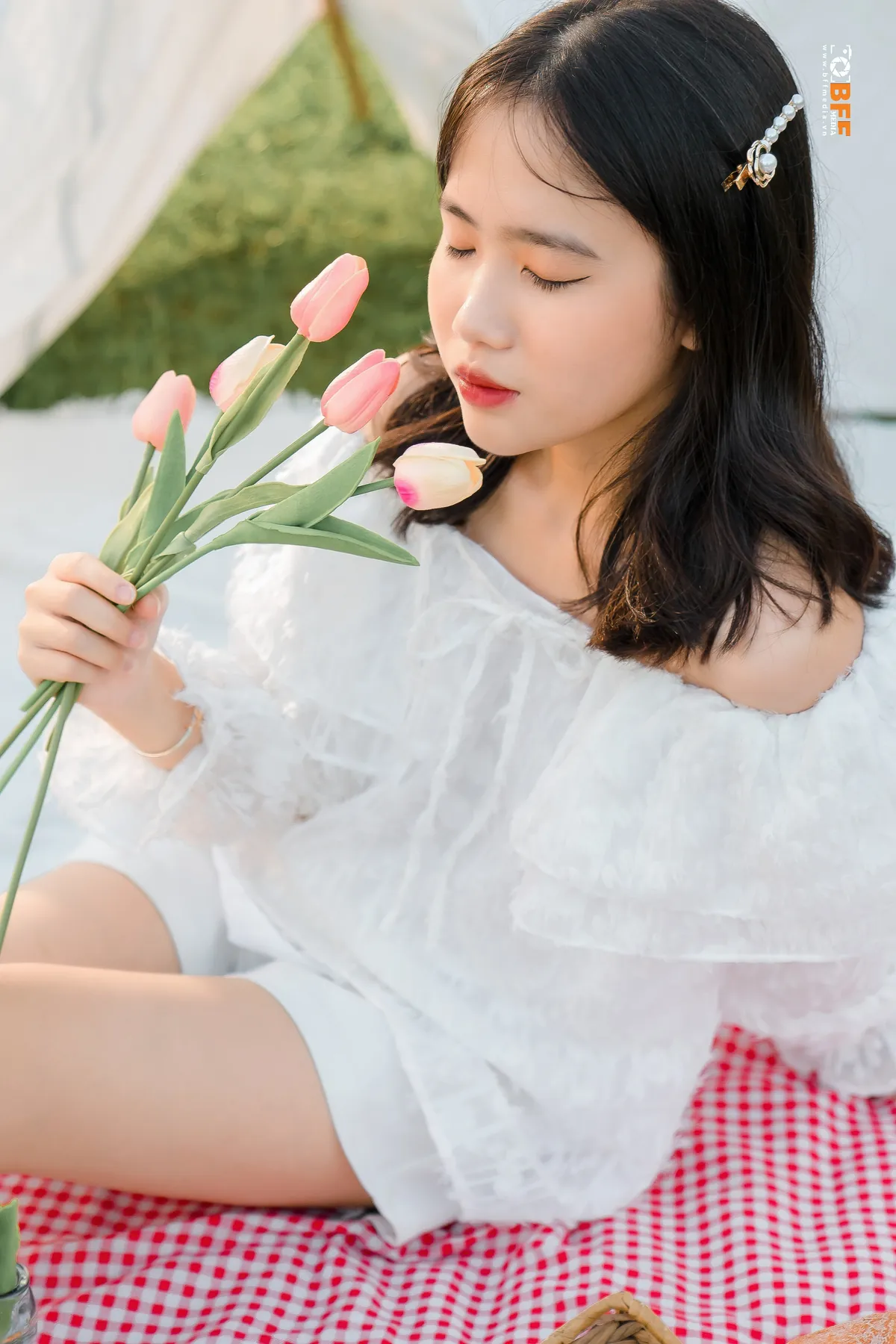 Nữ sinh váy trắng cầm bó tulip ngồi thảm picnic