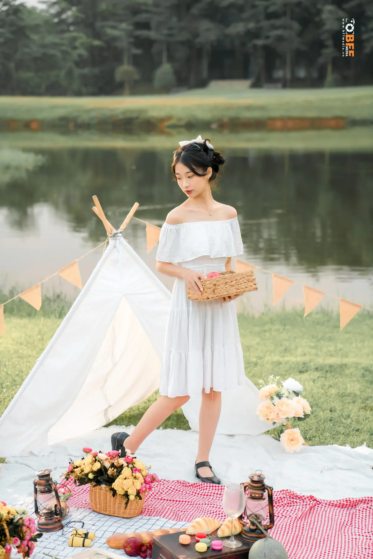 Nữ sinh váy liền trắng cầm giỏ hoa bên lều picnic