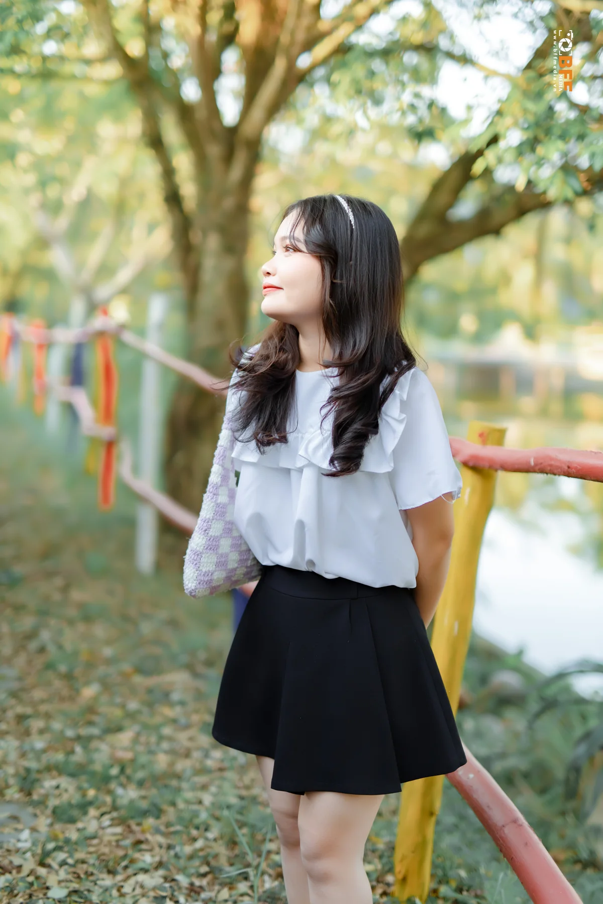 Nữ sinh áo sơ mi chân váy đen tạo dáng dựa lan can sân trường