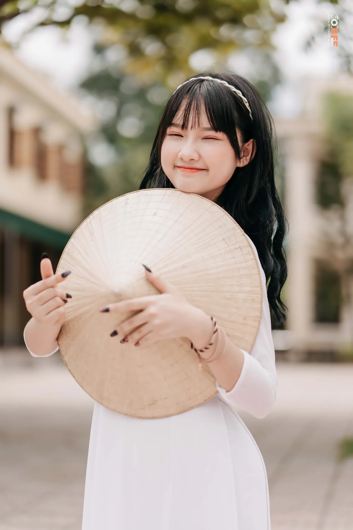 Nữ sinh áo dài trắng ôm nón lá tạo dáng cười tươi