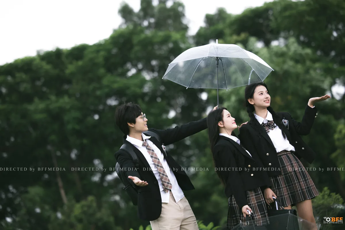 Một bạn nam che ô trong suốt cho hai bạn nữ cùng lớp khi chụp kỷ yếu ngoài trời