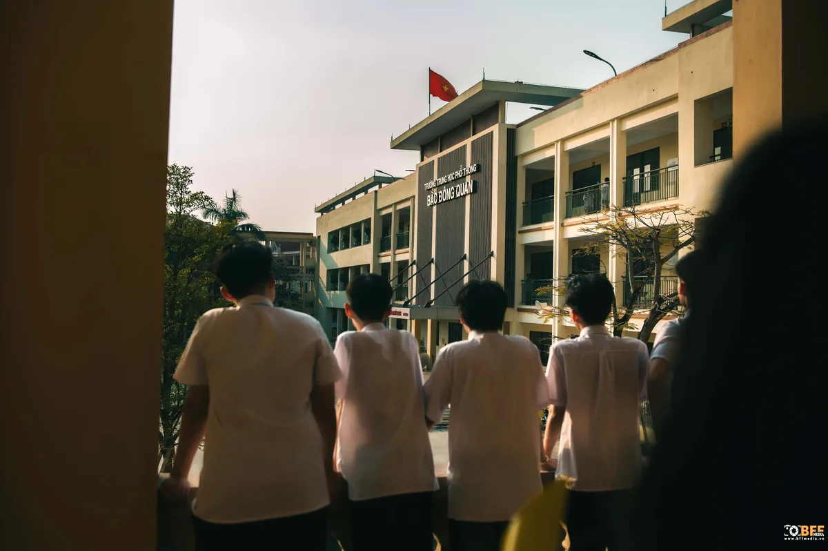 Nhóm học sinh đứng ở hành lang quay lưng nhìn về toà nhà trường trong khung hình cuối buổi chụp kỷ yếu