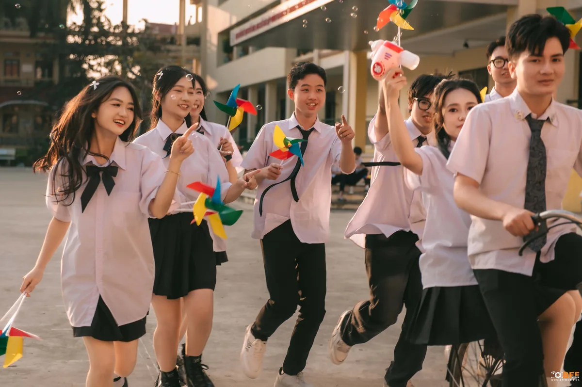 Học sinh cầm chong chóng chạy cười trên sân trường giữa buổi chụp kỷ yếu