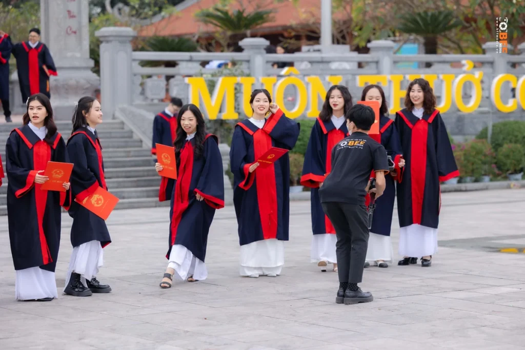Nhóm nữ sinh mặc áo cử nhân cầm bằng tốt nghiệp chụp kỷ yếu cuối năm học, nhiếp ảnh viên đang hướng dẫn tạo dáng