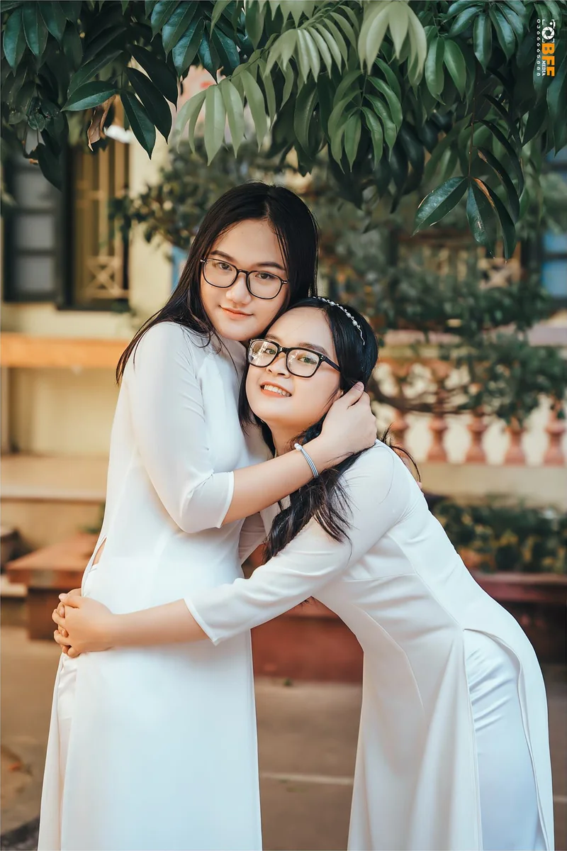 Hai bạn nữ mặc áo dài trắng ôm nhau trước dãy lớp học ngày bế giảng
