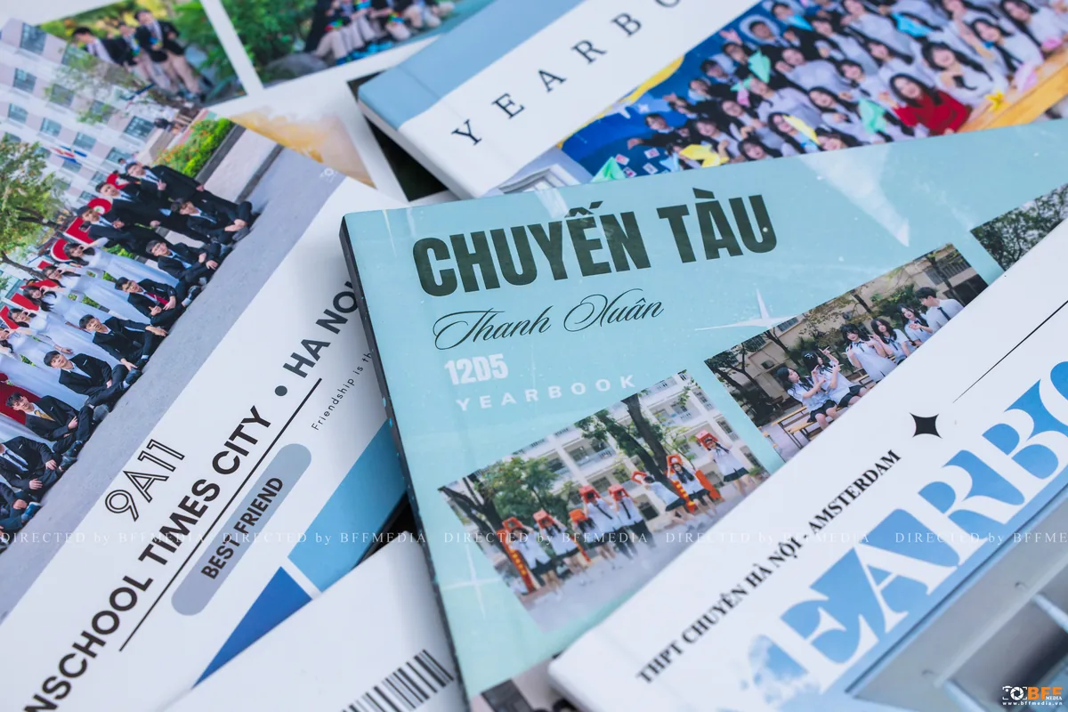 Những cuốn photobook kỷ yếu của các lớp xếp xoè trên bàn, bìa in ảnh tập thể và tên lớp