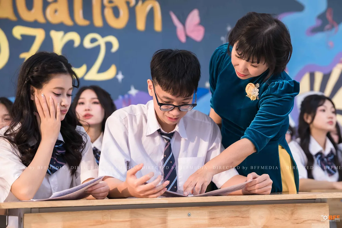 Cô giáo cúi xuống cùng học sinh đọc những trang giấy viết tay trong buổi chụp kỷ yếu