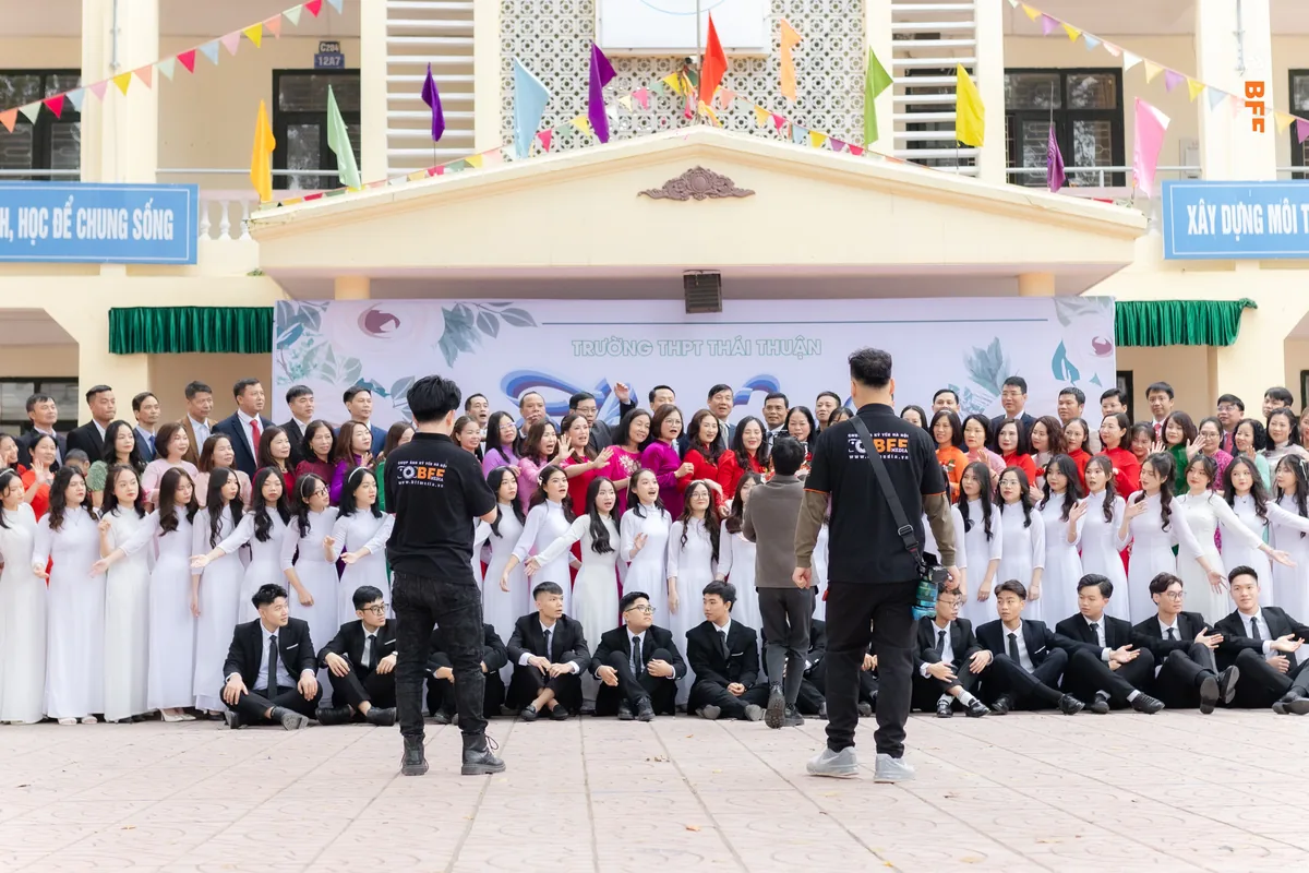 Hai thợ BFFMEDIA xếp đội hình ảnh tập thể kỷ yếu đông người trước phông lễ ở sân trường